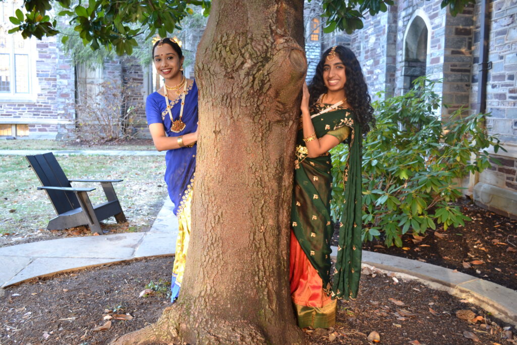 Samyukta Neeraj '25 and Vibha Srinivasan '26 peeking out from behind a tree