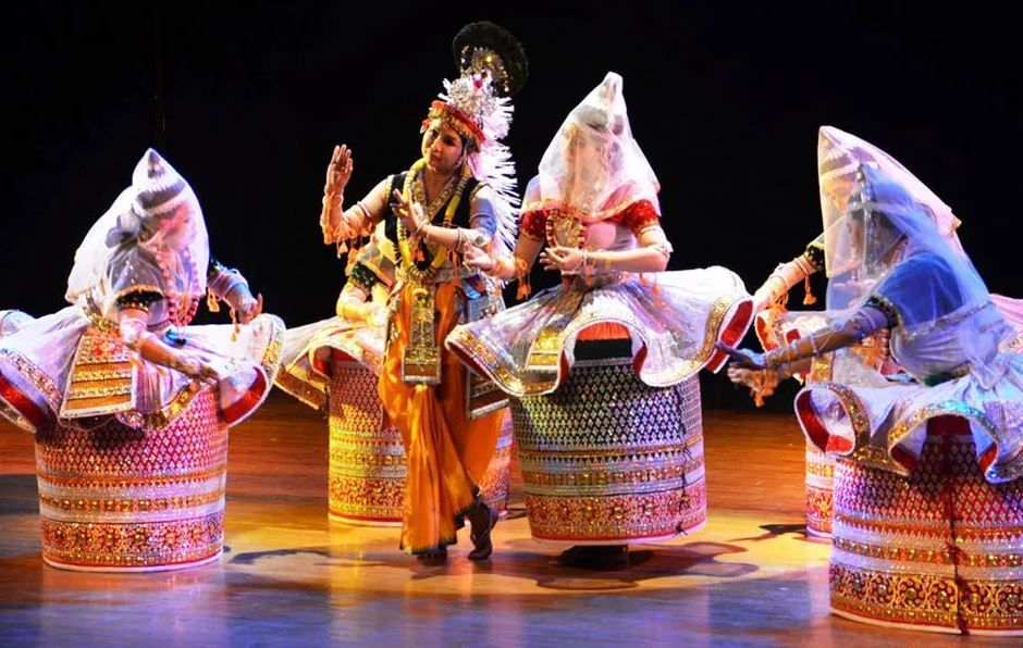5 manipuri dancers, four in large cylindrical dancers and one in a silk sari, mid scene