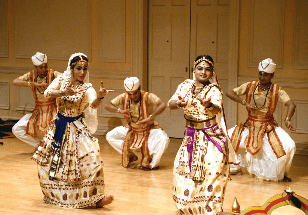 Five sattriya dancers in white costumes depicting a story with mudras (hand gestures)