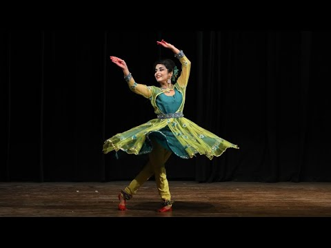 A kathak dancer in a green dress with her skirt expanding around her as she spins