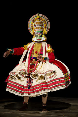 A kathakali dancer with their face painted green wearing a large white dress with red accents